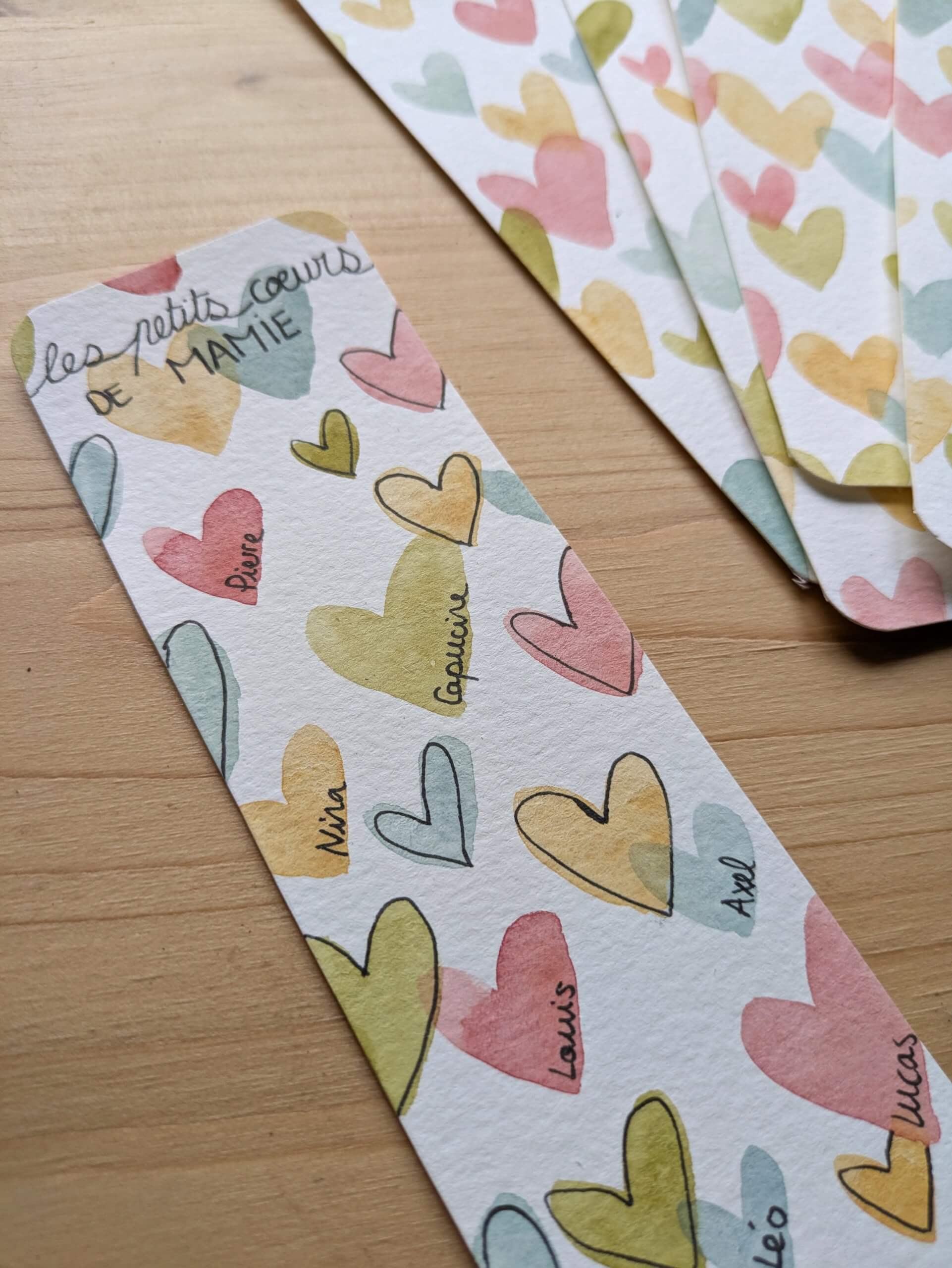 zoom sur un marque page illustré à l'aquarelle pour le fete des mamies représentant plein de petits coeurs colorés avec le prénom des petits enfants